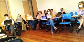 #fotopracegover, Sala de aula com alunos sentados pesquisando com notebooks na mesa, fim da descrição!